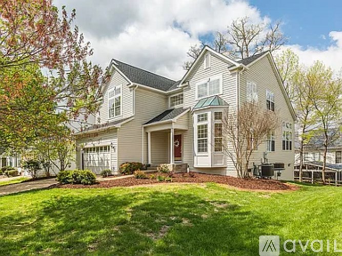 A large, two-story house with a front yard and a tree with red leaves.