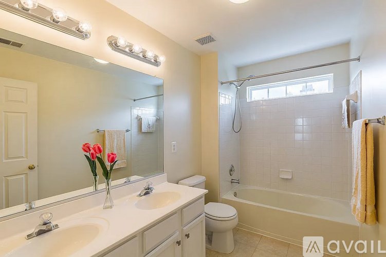 A bathroom with a white sink, toilet, and tub, and a mirror with lights above it.