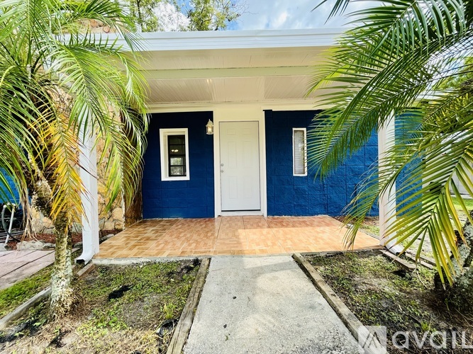 A blue house with a white door and windows surrounded by greenery.