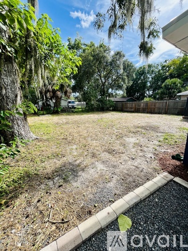 A backyard with a fence, trees, and a grassy area.