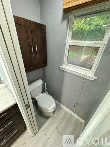 A bathroom with a toilet, a window, and a cabinet.