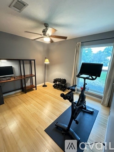 A room with a fan, a TV, a bicycle, and a window.