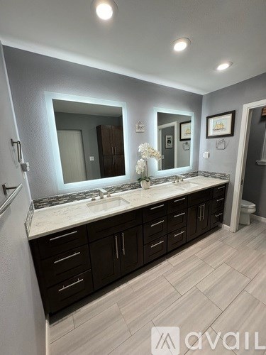 A bathroom with a large mirror and a sink with a marble countertop.