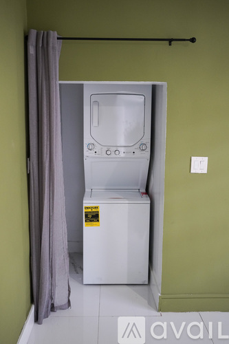 A washing machine is in a small room with a grey curtain.