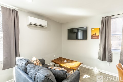 A living room with a grey couch, a wooden coffee table, and a flat screen TV mounted on the wall.