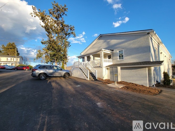 A silver car is parked in front of a house with a tree to the left.