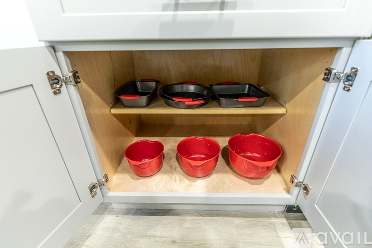 A kitchen cabinet with three red bowls and two black bowls inside.