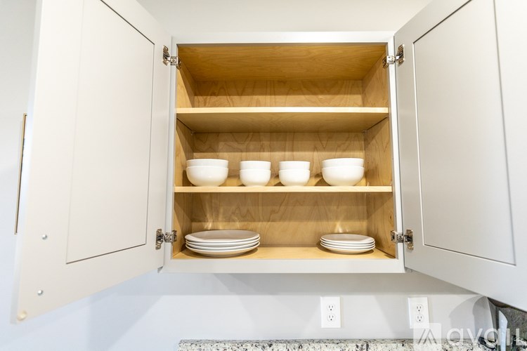 A kitchen cabinet is open, revealing shelves with bowls and plates.