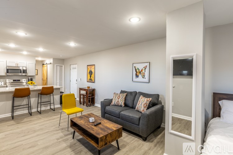 A living room with a grey couch, a coffee table, and a kitchen area in the background.