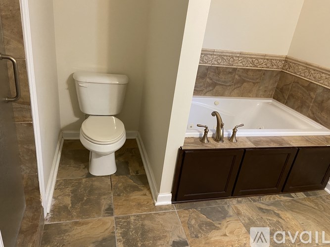 A white toilet is in a bathroom with a brown cabinet and a bathtub.
