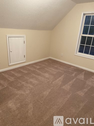 A room with a carpeted floor and a window with a white frame.