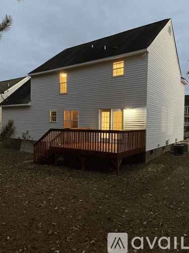 A white house with a black roof and a wooden deck.