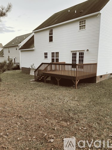 A white house with a brown deck in the front yard.
