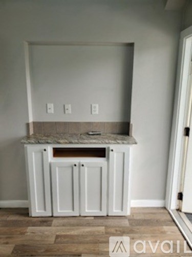 A white cabinet with a marble top is in a room with a light grey wall.