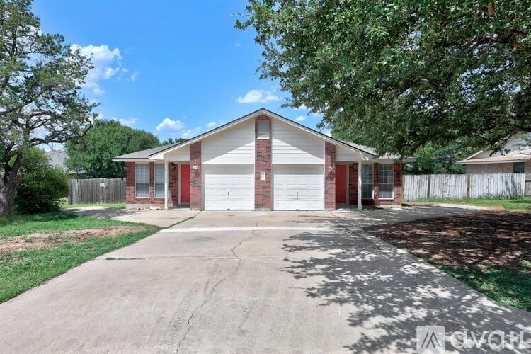 A house with a red garage door is surrounded by a fence and trees.