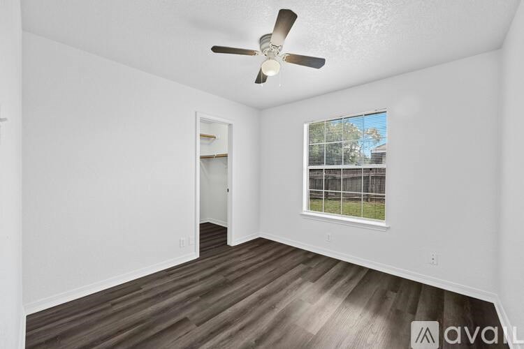 A room with a ceiling fan and a window overlooking a fence.