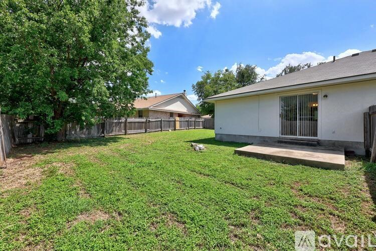 A backyard with a white house, a tree, and a fence.