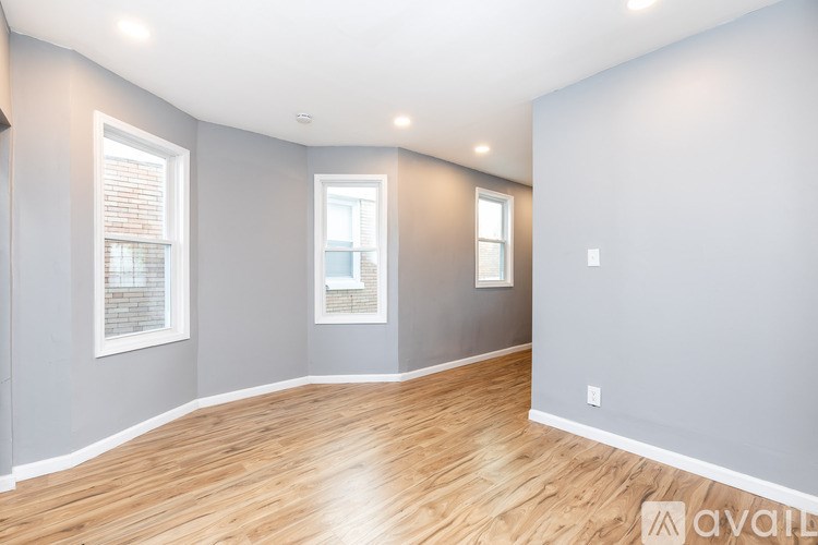 A spacious room with wooden floors and two windows.