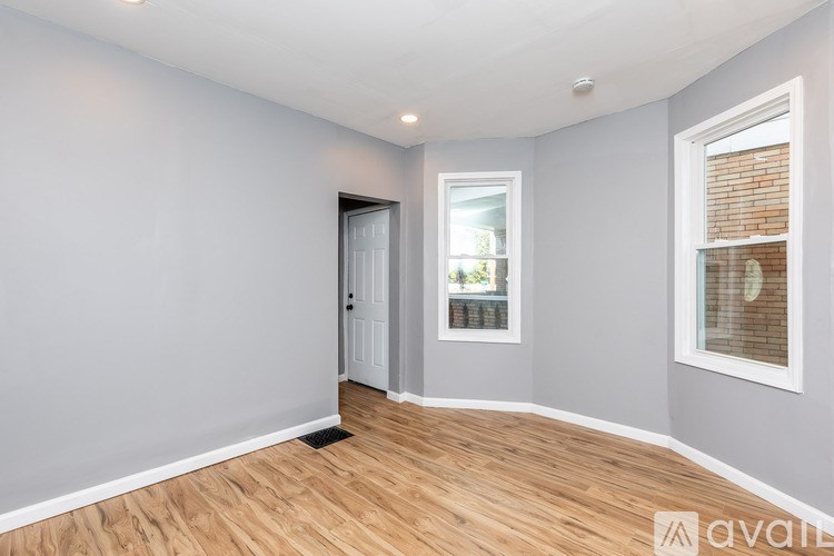 A room with wooden flooring and two windows with blinds.