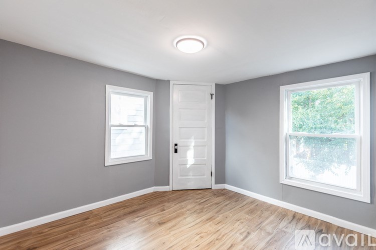 A room with a white door, two windows, and wooden flooring.