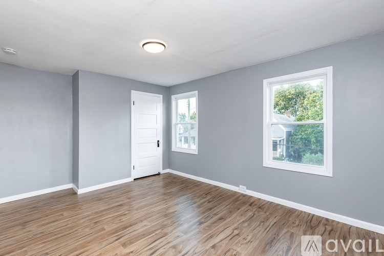 A spacious room with wooden flooring and two windows.