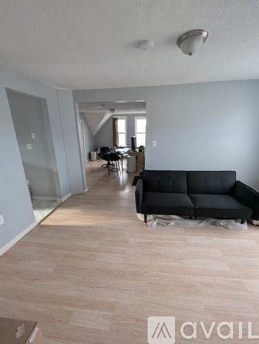 A living room with a black couch and a dining area in the background.
