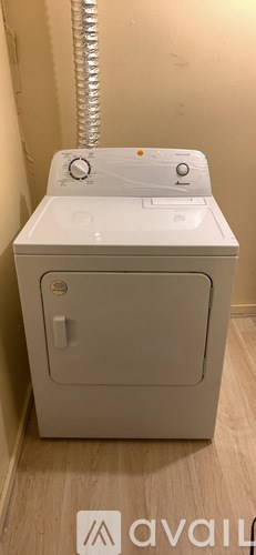 A white washing machine in a room with a pipe on the wall.