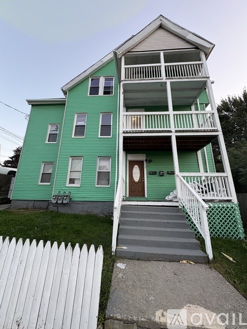 A green two-story house with a white picket fence.