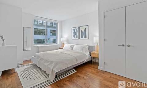 A bedroom with a bed, a nightstand, and a window with a view of a building outside.