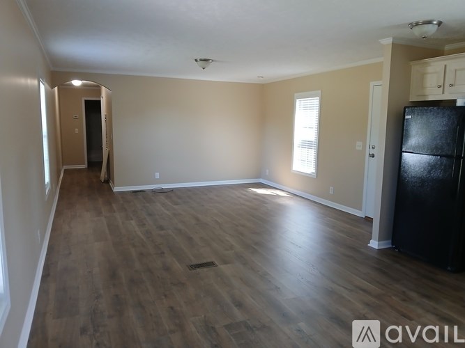 A spacious room with wooden flooring and a black refrigerator.