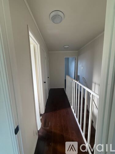 A hallway with a white railing and wooden floor.