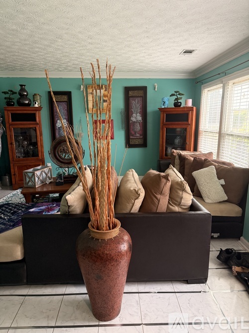 A brown vase with tall thin sticks in it sits on a table.