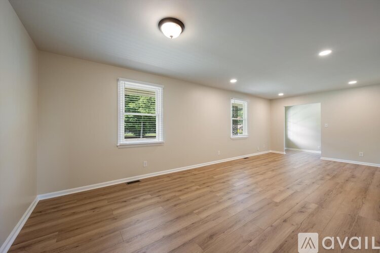 A spacious room with wooden flooring and a window with blinds.