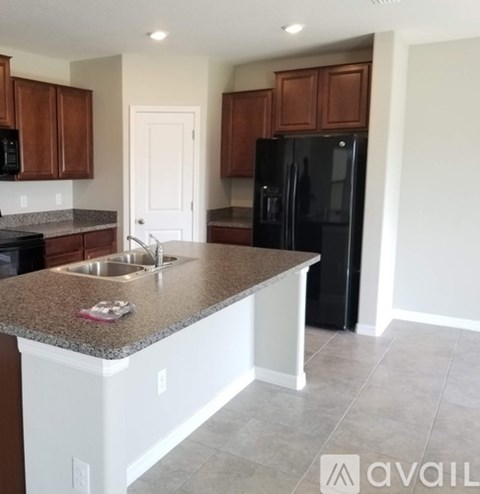 A kitchen with a black refrigerator and brown cabinets.