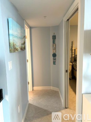 A hallway with a painting on the wall and a doorway leading to another room.