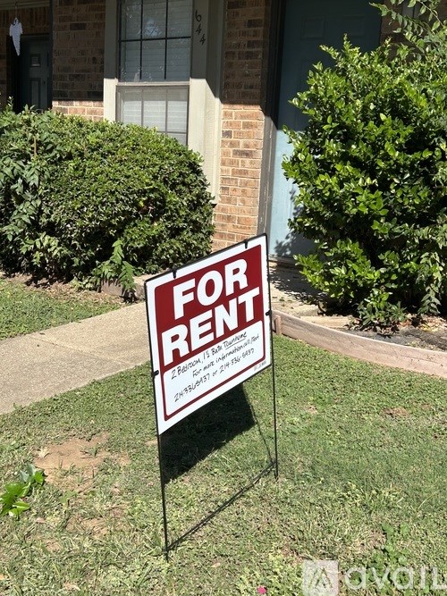 A red and white for rent sign is placed in front of a house.