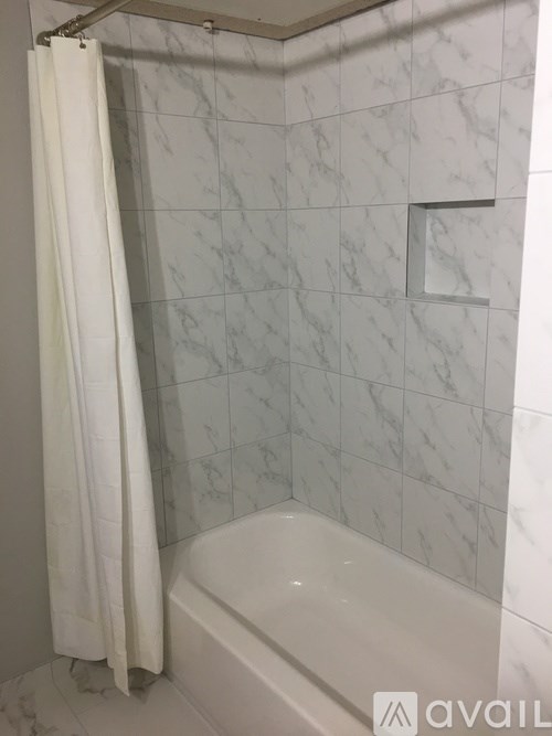 A white shower curtain hangs over a white bathtub in a marble tiled bathroom.