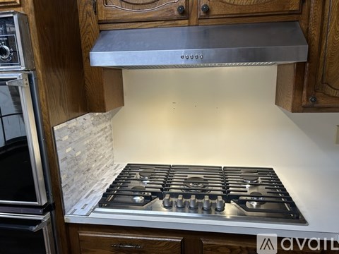 A stainless steel stove top is installed in a kitchen with wooden cabinets.