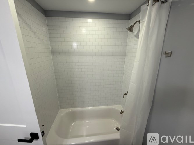 A white tiled bathroom with a white bathtub and shower curtain.