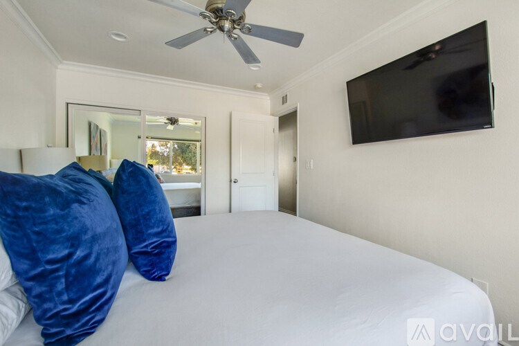 A bedroom with a bed, a ceiling fan, and a flat screen TV mounted on the wall.