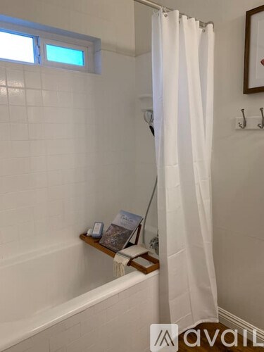 A white shower curtain hangs in a white tiled bathroom.