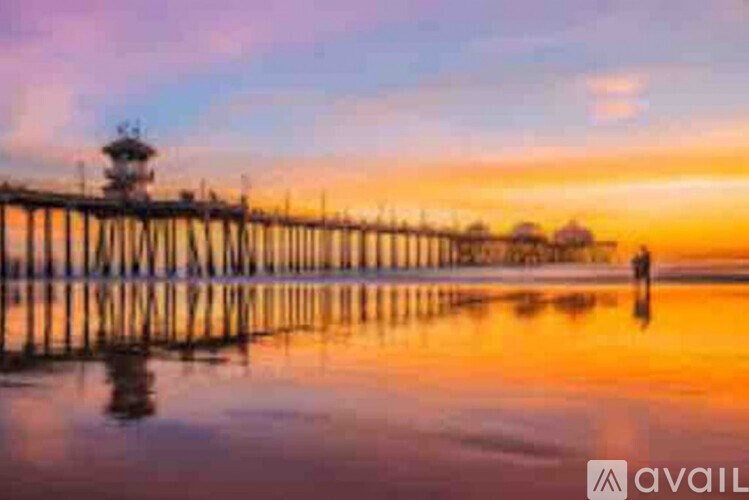 A person stands on a pier with a lighthouse in the background during a sunset.