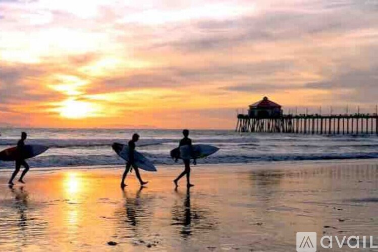 Three people are walking on the beach with surfboards, heading towards a pier.