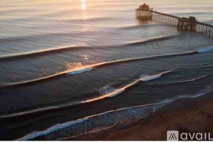 A sunset view of a beach with waves gently lapping at the shore and a pier in the distance.