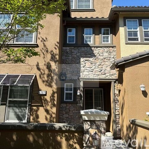 A stone pillar is in front of a tan building with a window.