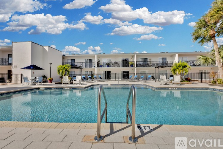 A large swimming pool in front of a building with a metal railing and a palm tree.