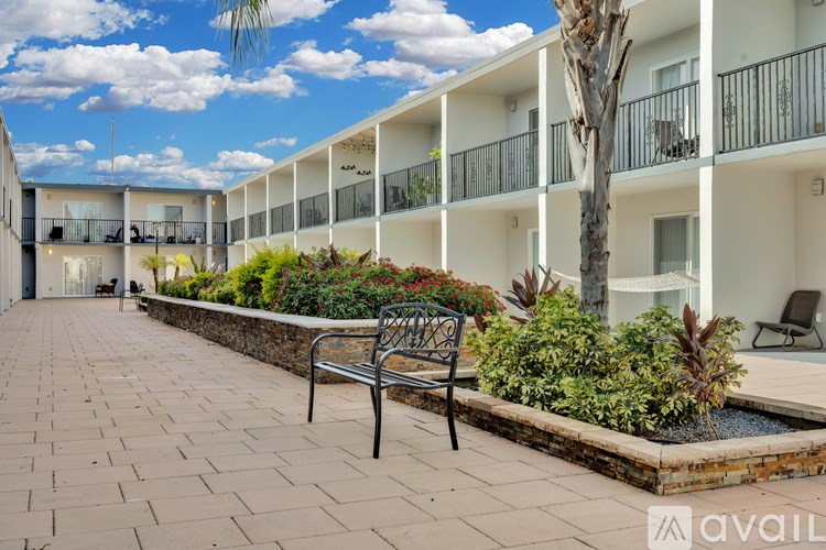 A bench is on a brick walkway in front of a building with balconies.