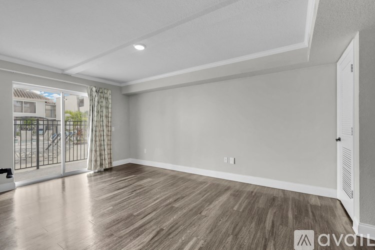 A spacious room with wooden flooring and a sliding glass door leading to a balcony.