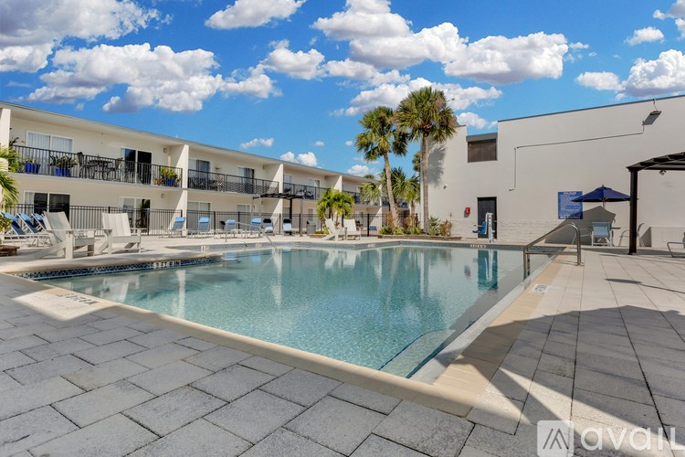 A large swimming pool surrounded by a tiled patio and a building with balconies.