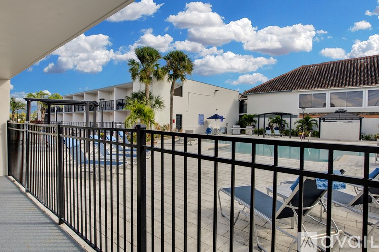 A balcony with a black railing overlooks a pool and palm trees.